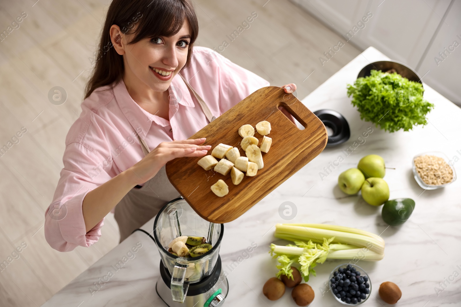 Photo of Young woman making delicious smoothie with blender at white marble table in kitchen, above view