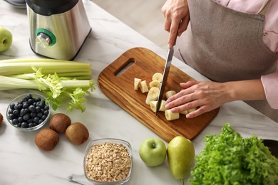 Photo of Woman making delicious smoothie with blender at white marble table in kitchen, closeup