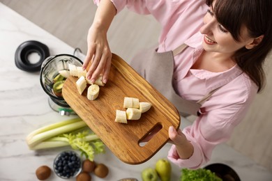 Young woman making delicious smoothie with blender at white marble table in kitchen, top view