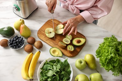 Woman cutting apple for smoothie at white marble table in kitchen, closeup