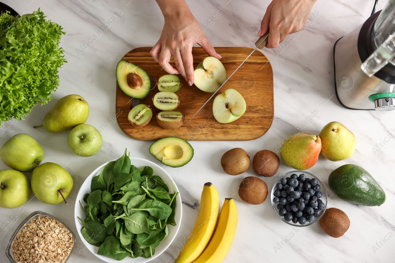 Photo of Woman making delicious smoothie with blender at white marble table in kitchen, top view