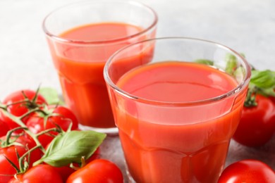 Photo of Tasty tomato juice in glasses, basil and fresh vegetables on table, closeup