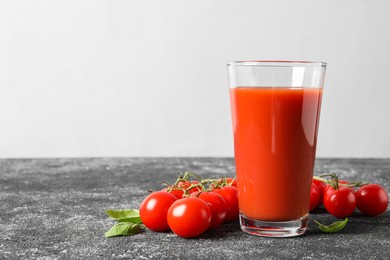 Photo of Tasty tomato juice in glass, basil and fresh vegetables on grey table, space for text