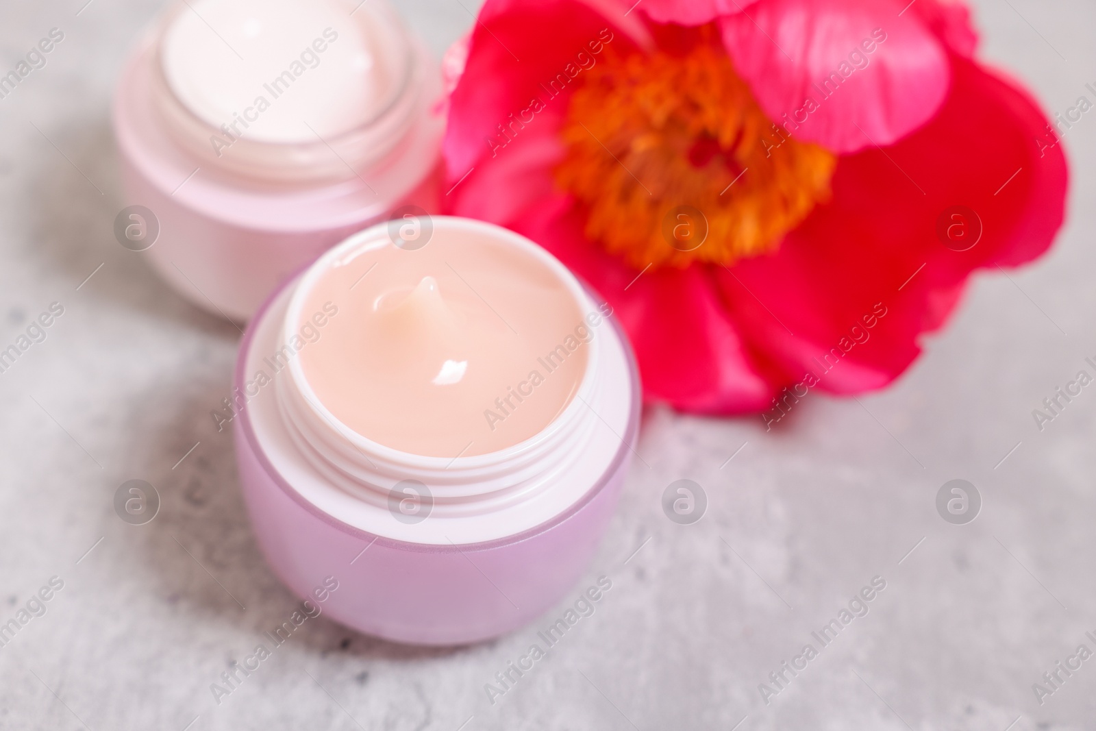 Photo of Jars of creams and peony flower on gray table, closeup