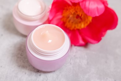 Jars of creams and peony flower on gray table, closeup