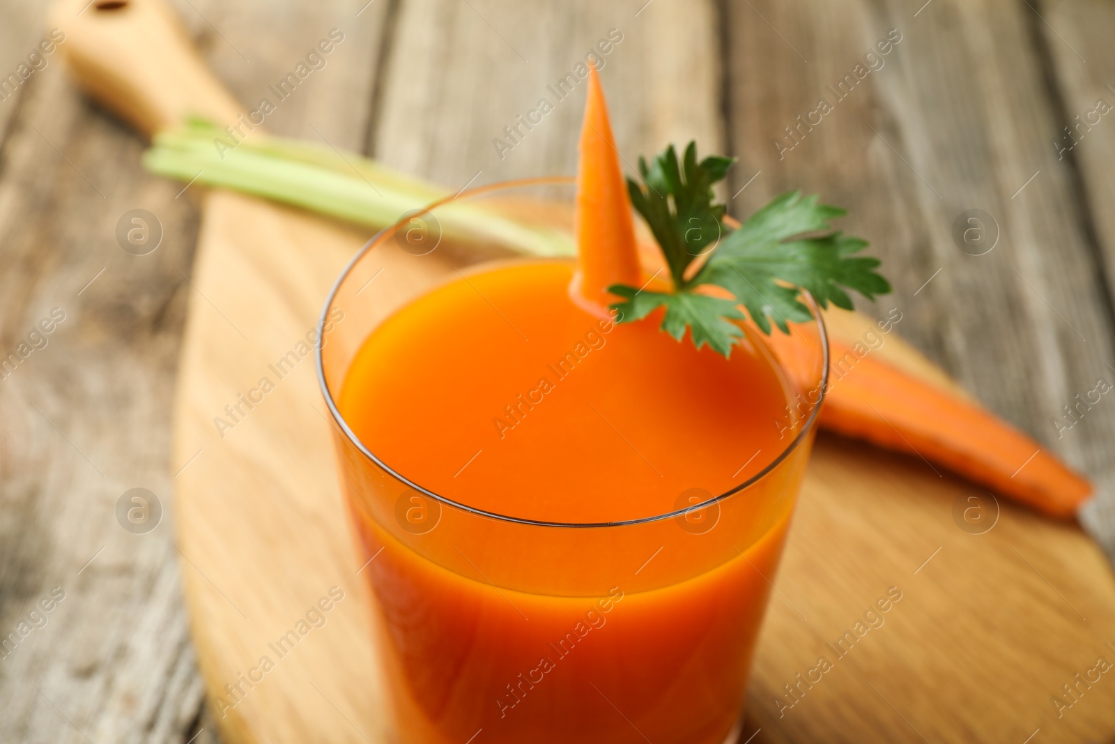 Photo of Healthy juice in glass and fresh carrot on wooden table, closeup