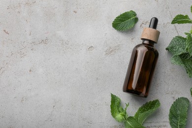 Photo of Bottle of essential oil and mint on light textured table, flat lay. Space for text