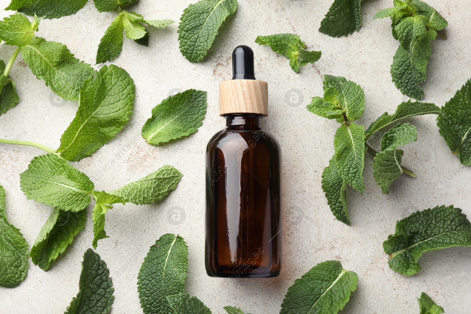 Photo of Bottle of essential oil and mint on light textured table, flat lay