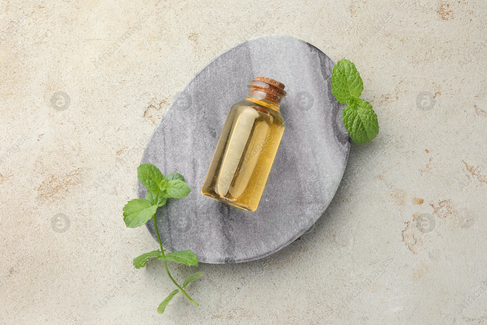 Photo of Bottle of essential oil and mint on light textured table, top view