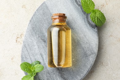 Photo of Bottle of essential oil and mint on light textured table, top view