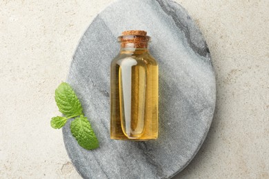 Photo of Bottle of essential oil and mint on light textured table, top view