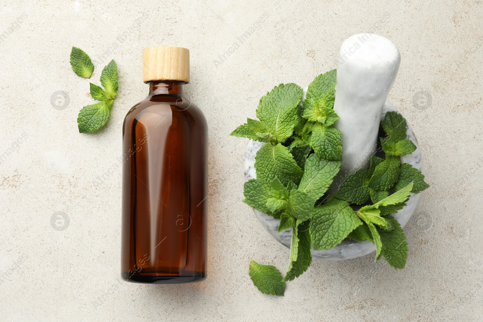 Photo of Bottle of essential oil, mint, mortar and pestle on light textured table, top view