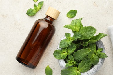 Bottle of essential oil and mint on light textured table, flat lay