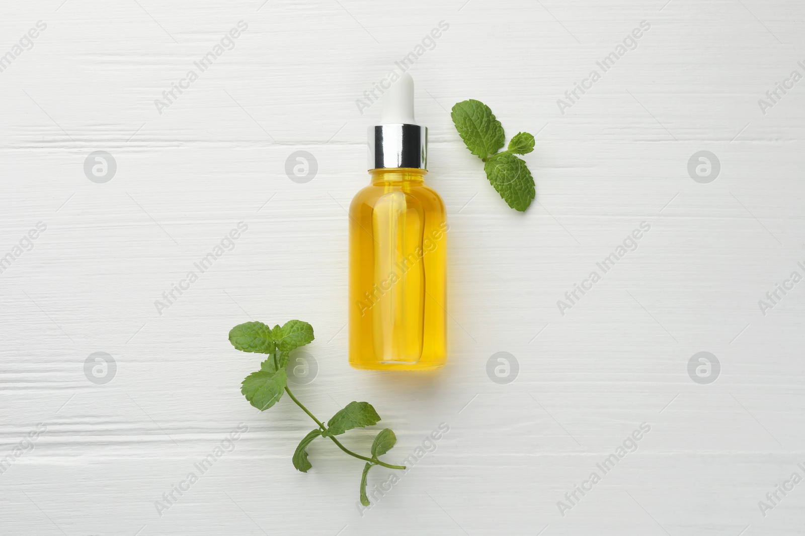 Photo of Bottle of essential oil and mint on white wooden table, flat lay