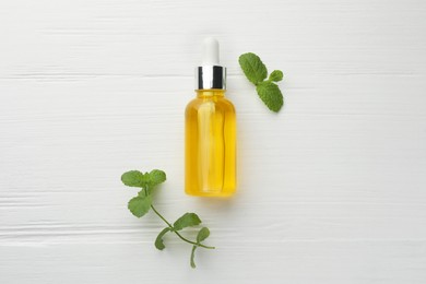 Photo of Bottle of essential oil and mint on white wooden table, flat lay