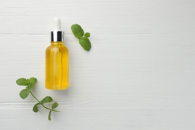 Photo of Bottle of essential oil and mint on white wooden table, flat lay. Space for text