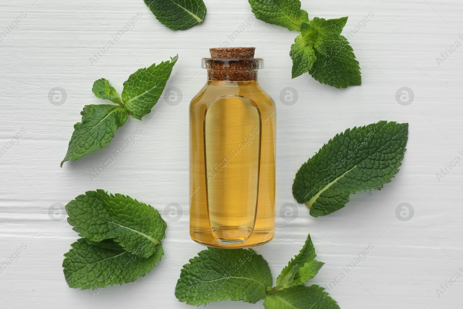 Photo of Bottle of essential oil and mint on white wooden table, flat lay