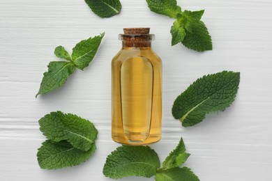 Bottle of essential oil and mint on white wooden table, flat lay