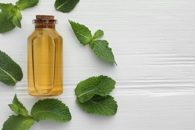 Photo of Bottle of essential oil and mint on white wooden table, flat lay. Space for text