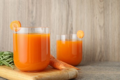 Healthy carrot juice in glasses and vegetables on wooden table, space for text