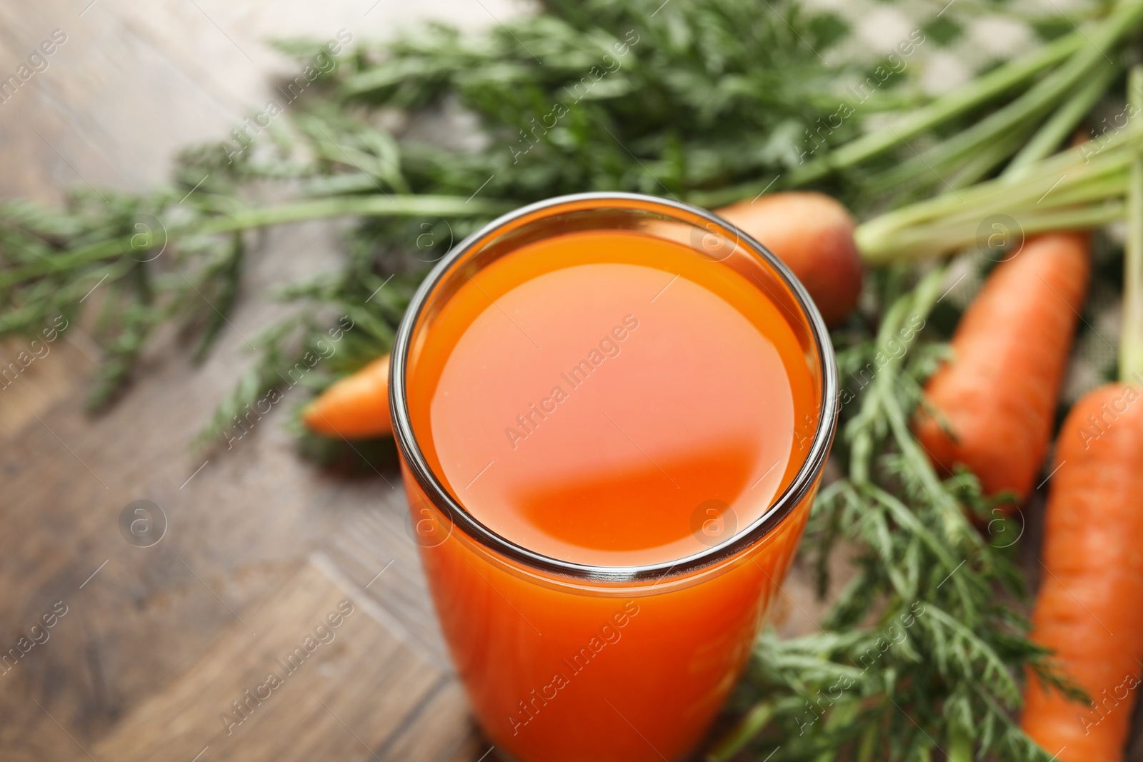 Photo of Healthy carrot juice in glass and fresh vegetables on wooden table, closeup