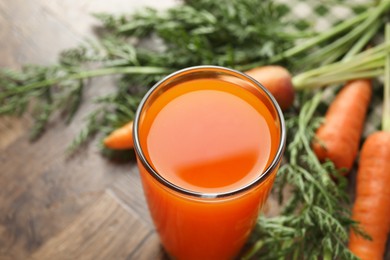 Photo of Healthy carrot juice in glass and fresh vegetables on wooden table, closeup