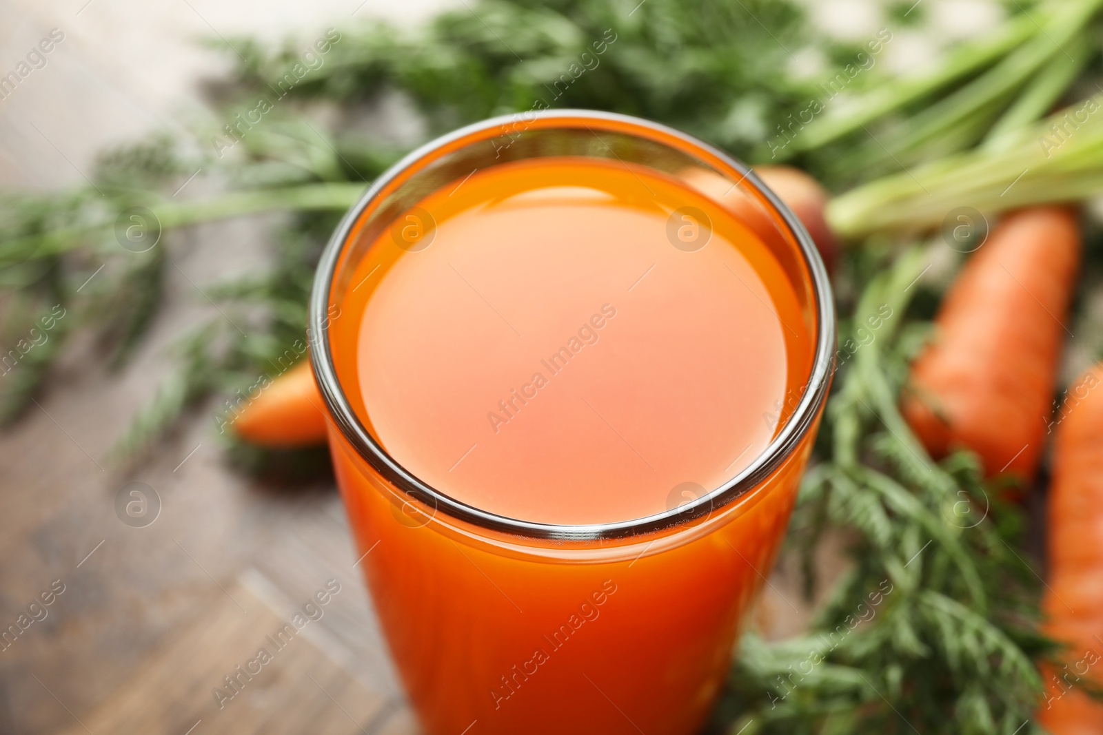 Photo of Healthy carrot juice in glass and fresh vegetables on table, closeup