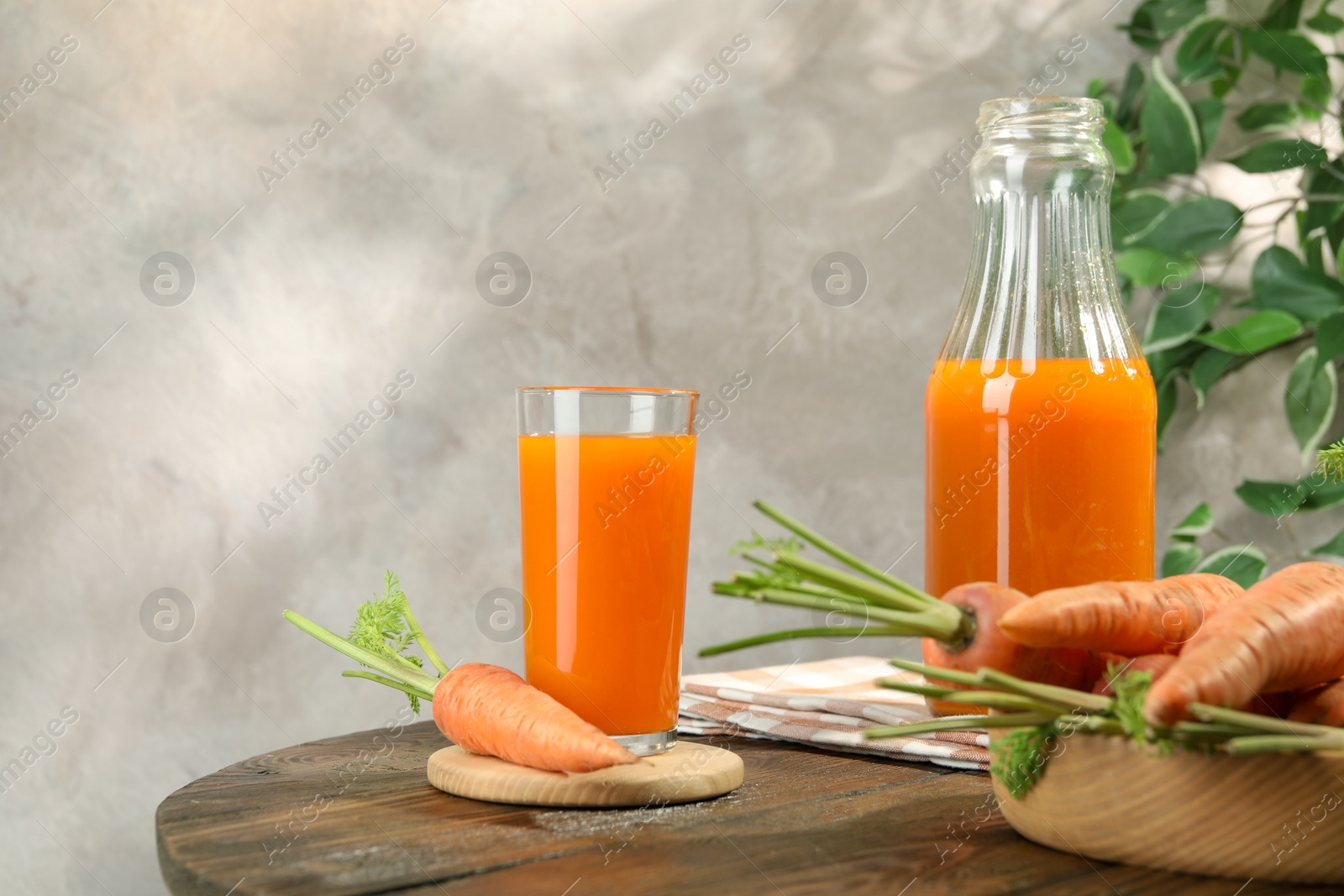 Photo of Healthy carrot juice in glass, bottle and fresh vegetables on wooden table