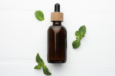 Bottle of mint essential oil and fresh leaves on white wooden table, top view