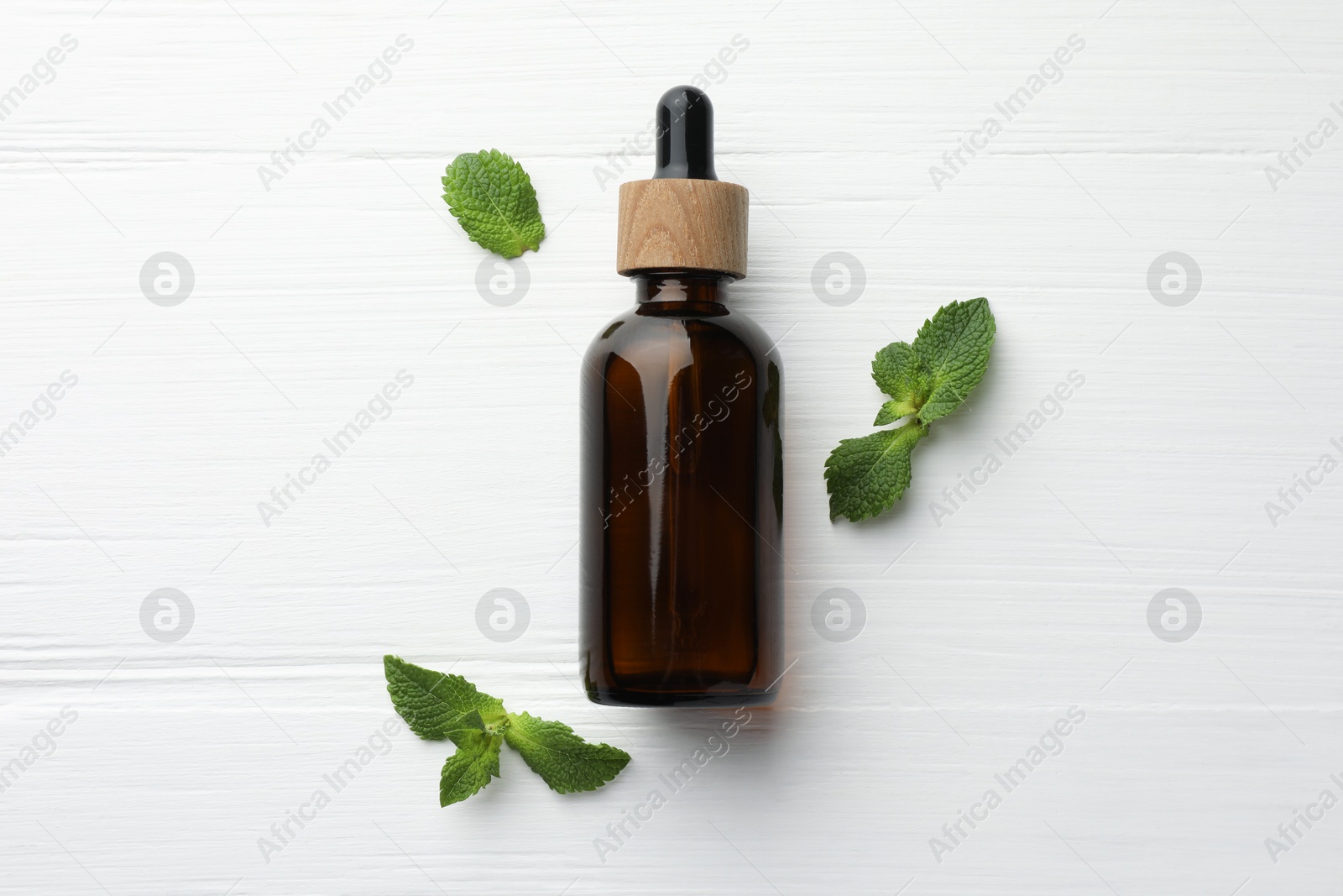 Photo of Bottle of mint essential oil and fresh leaves on white wooden table, top view