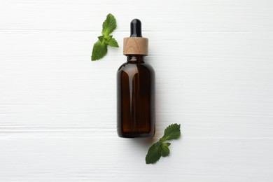 Photo of Bottle of mint essential oil and fresh leaves on white wooden table, top view