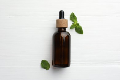 Photo of Bottle of mint essential oil and fresh leaves on white wooden table, top view