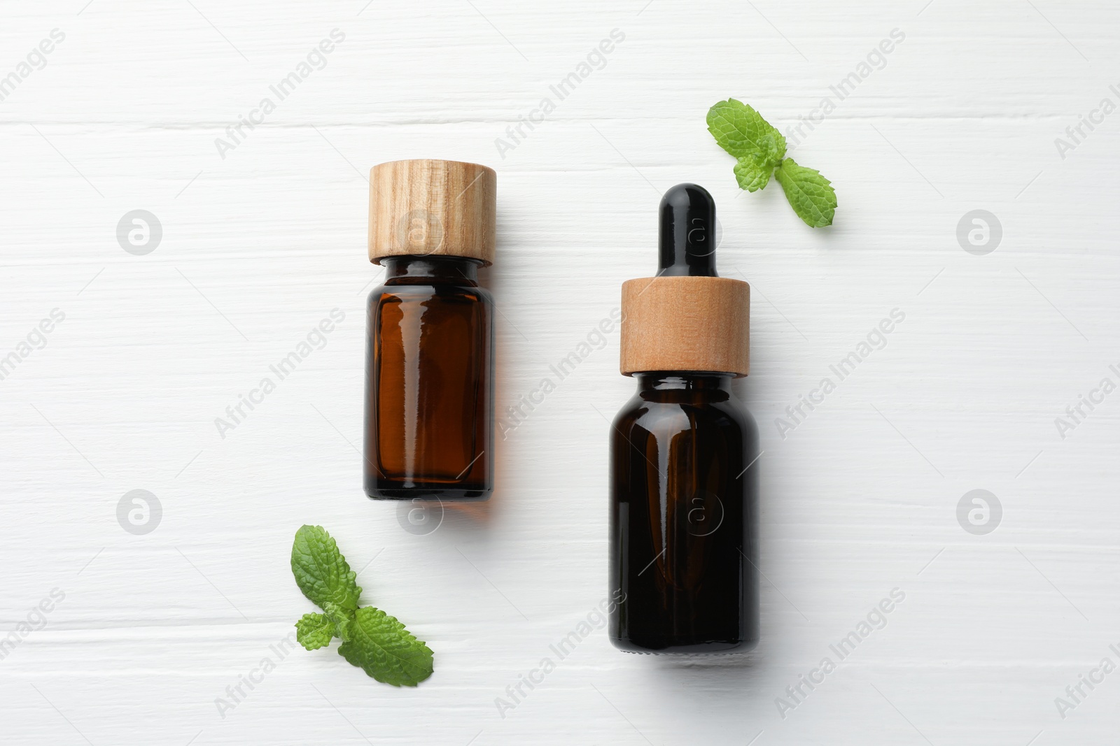 Photo of Bottles of mint essential oil and fresh leaves on white wooden table, top view