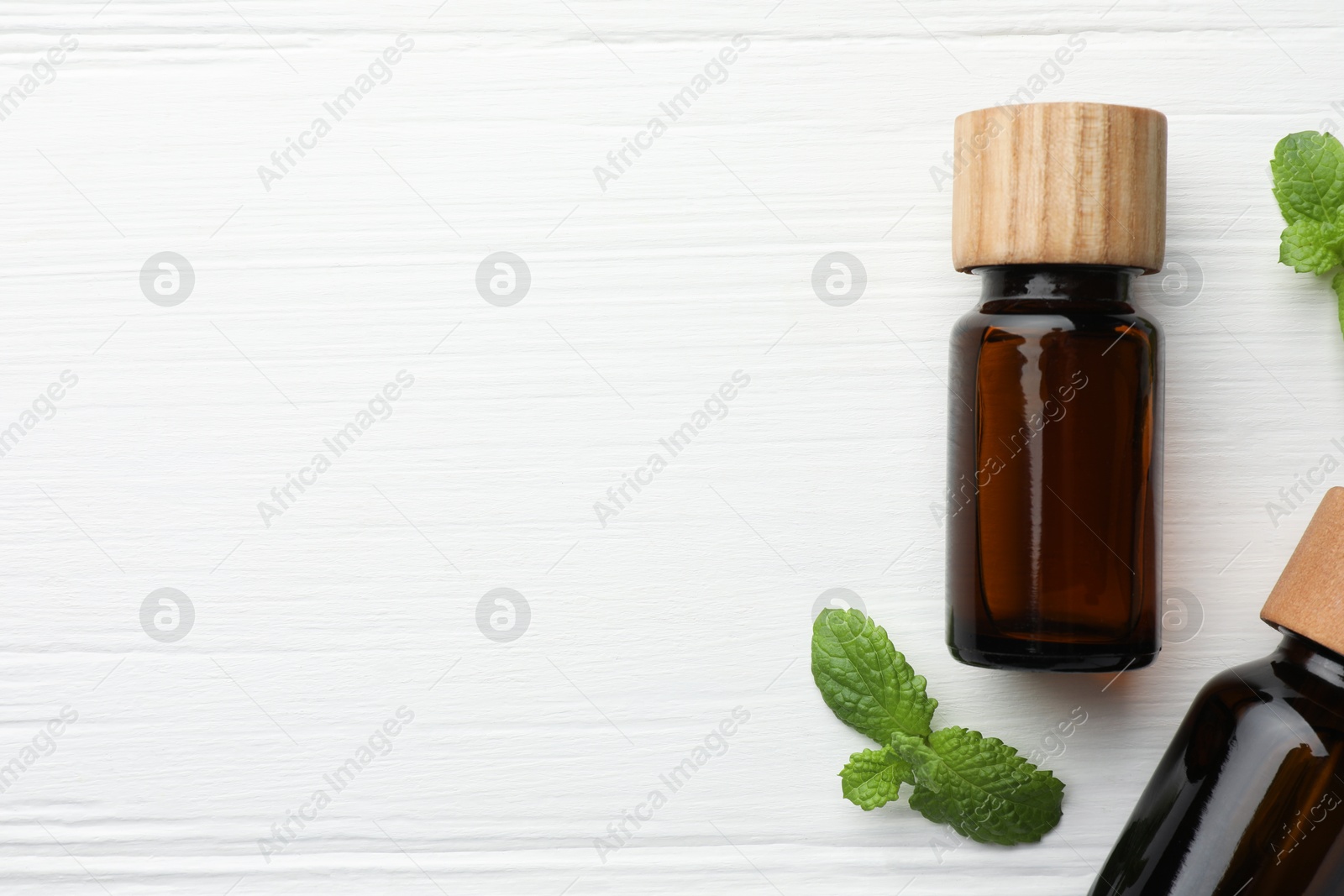 Photo of Bottles of mint essential oil and fresh leaves on white wooden table, top view. Space for text