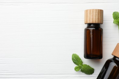 Photo of Bottles of mint essential oil and fresh leaves on white wooden table, top view. Space for text