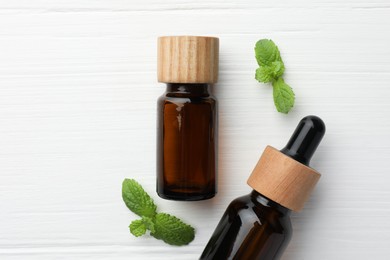 Photo of Bottles of mint essential oil and fresh leaves on white wooden table, top view