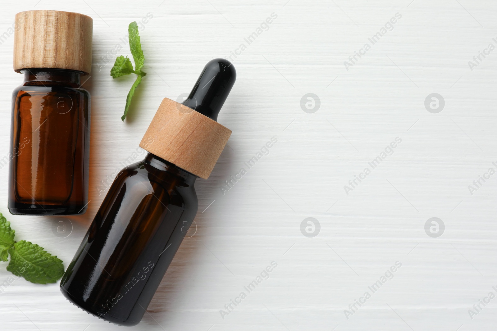 Photo of Bottles of mint essential oil and fresh leaves on white wooden table, top view. Space for text