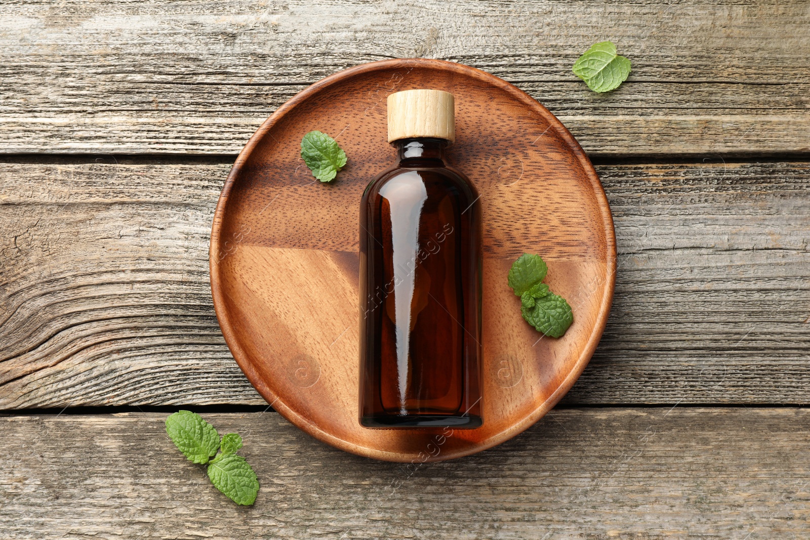 Photo of Bottle of mint essential oil and fresh leaves on wooden table, top view