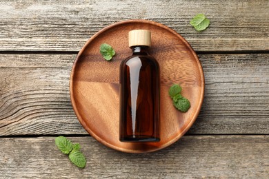 Bottle of mint essential oil and fresh leaves on wooden table, top view