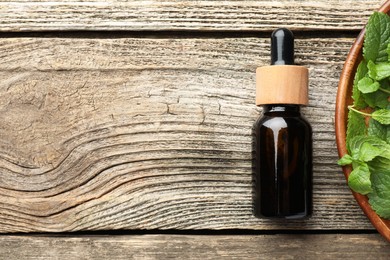 Photo of Bottle of mint essential oil and fresh leaves on wooden table, top view. Space for text