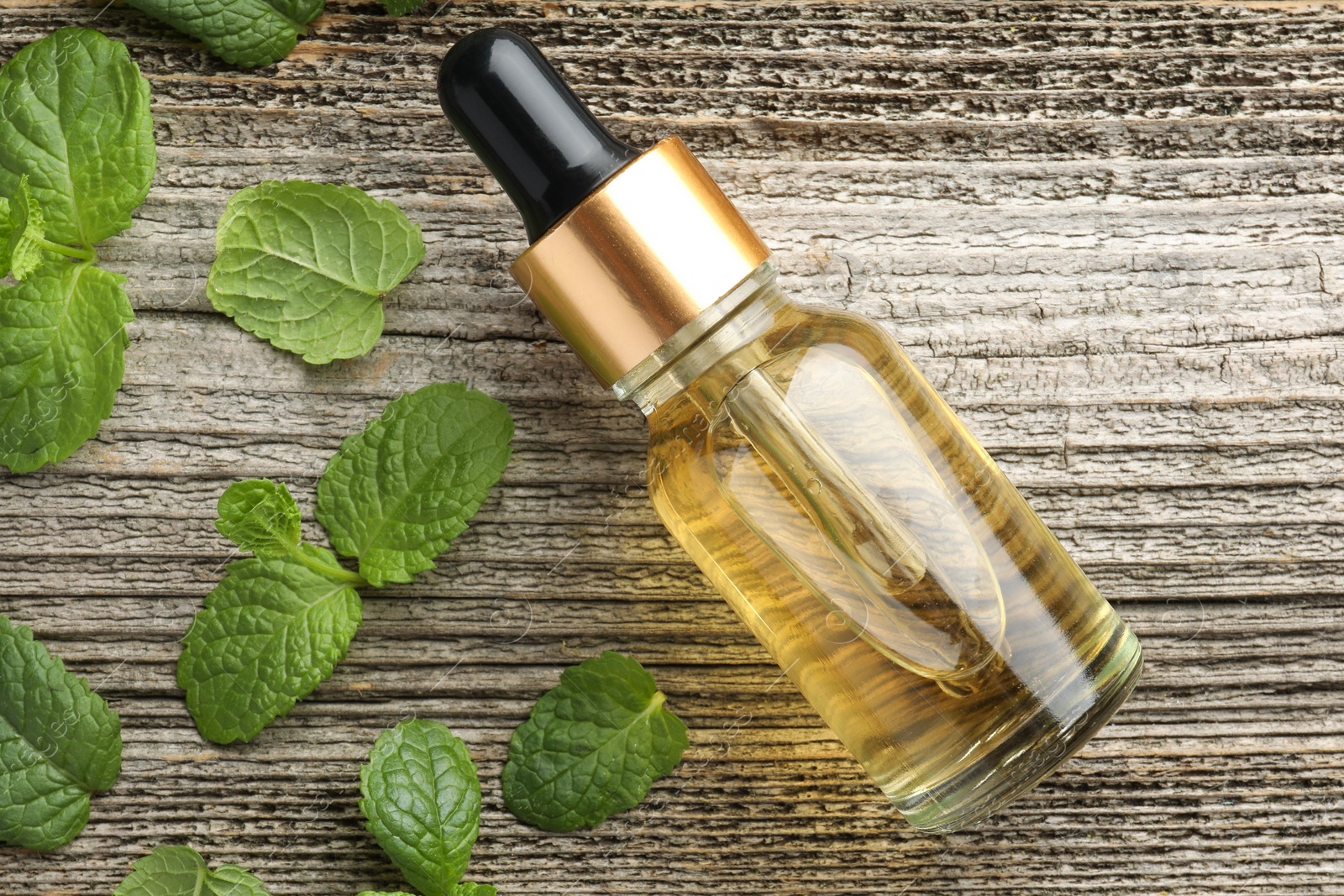 Photo of Bottle of mint essential oil and fresh leaves on wooden table, top view