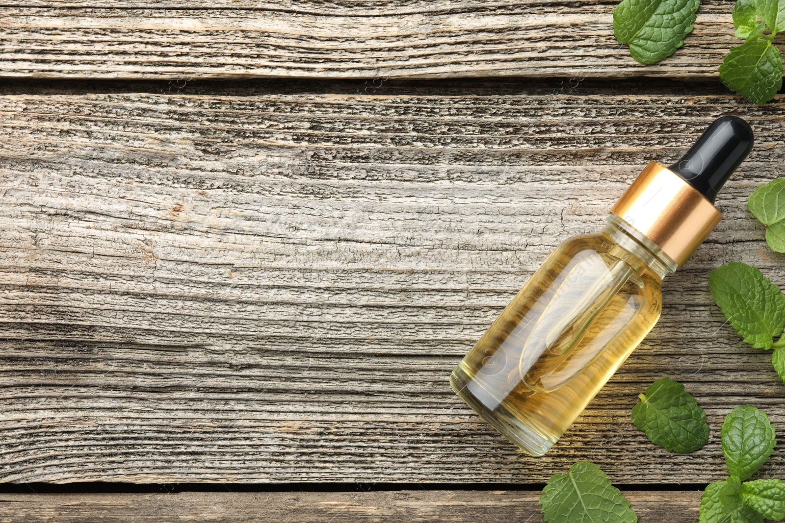 Photo of Bottle of mint essential oil and fresh leaves on wooden table, top view. Space for text