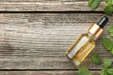 Photo of Bottle of mint essential oil and fresh leaves on wooden table, top view. Space for text