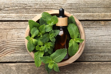 Bottle of mint essential oil and fresh leaves on wooden table, top view