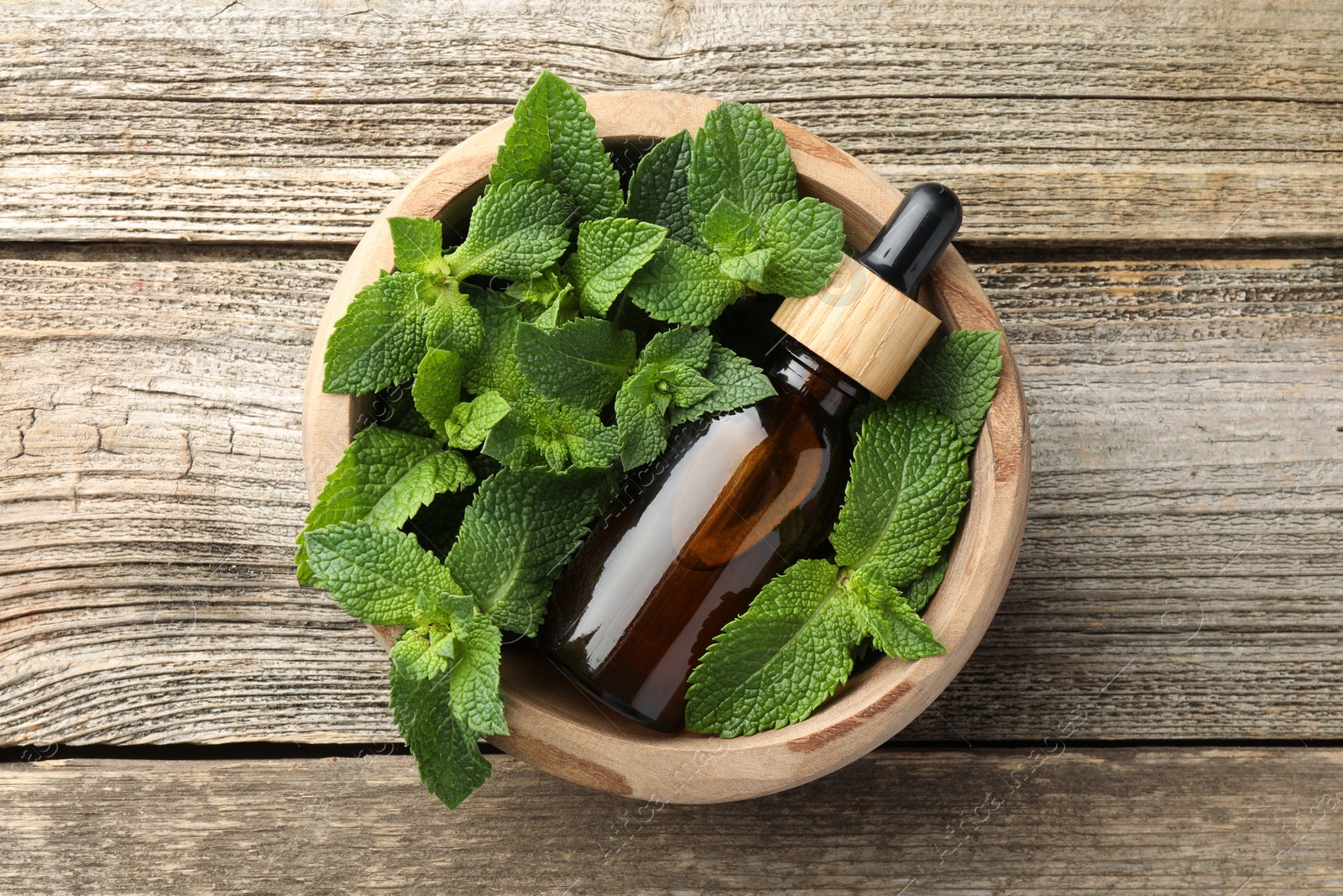 Photo of Bottle of mint essential oil and fresh leaves on wooden table, top view