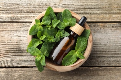 Photo of Bottle of mint essential oil and fresh leaves on wooden table, top view