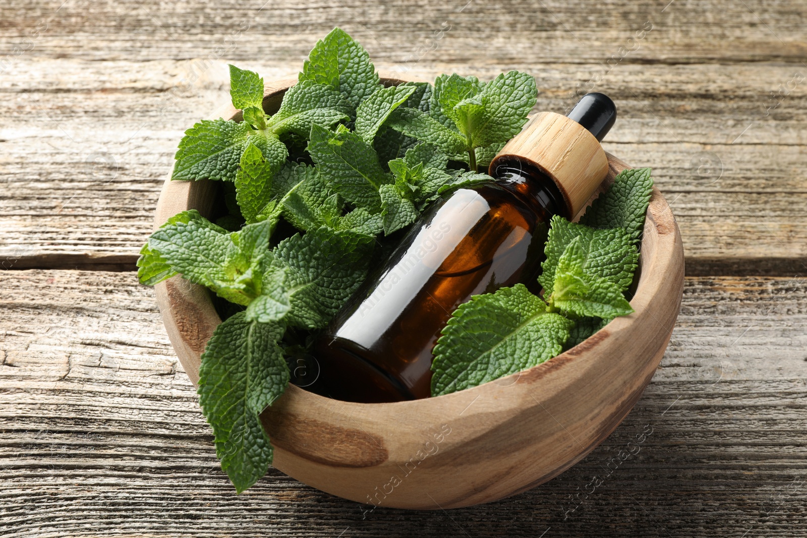 Photo of Bottle of mint essential oil and fresh leaves on wooden table