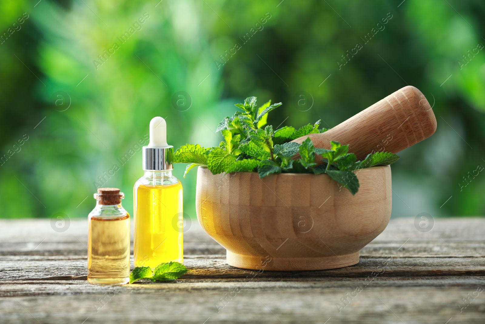 Photo of Bottles of mint essential oil and fresh leaves on wooden table