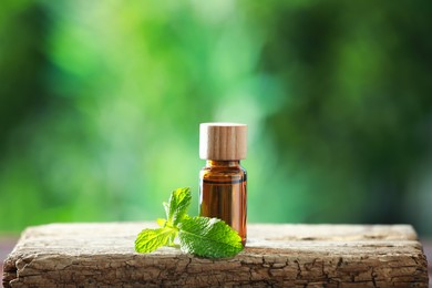 Photo of Bottle of mint essential oil and fresh leaves on wooden table