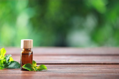 Photo of Bottle of mint essential oil and fresh leaves on wooden table, space for text